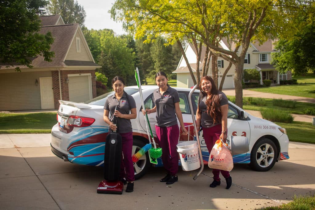 tessa cleaning workers holding cleaning supplies smiling in front of car